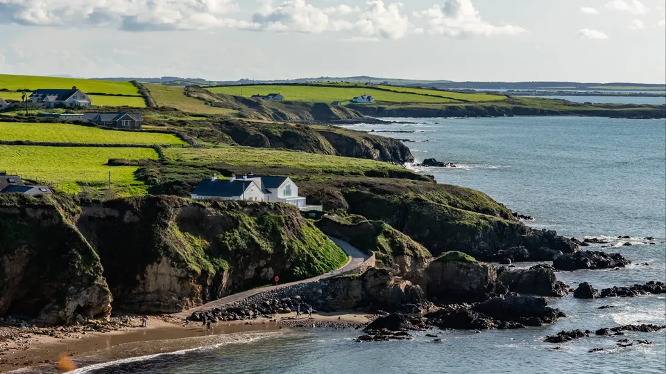 Coastal cliffs with white house perched on hillside above rocky beach.