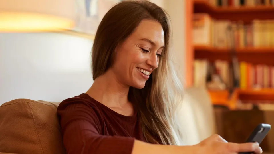 Frau schaut lächelnd auf Smartphone.