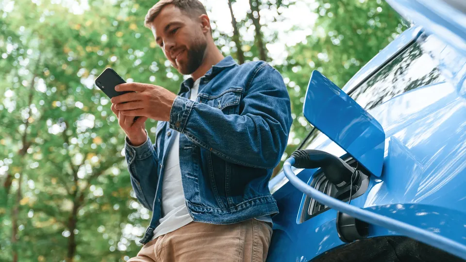 Uomo che tiene uno smartphone mentre ricarica un veicolo elettrico.