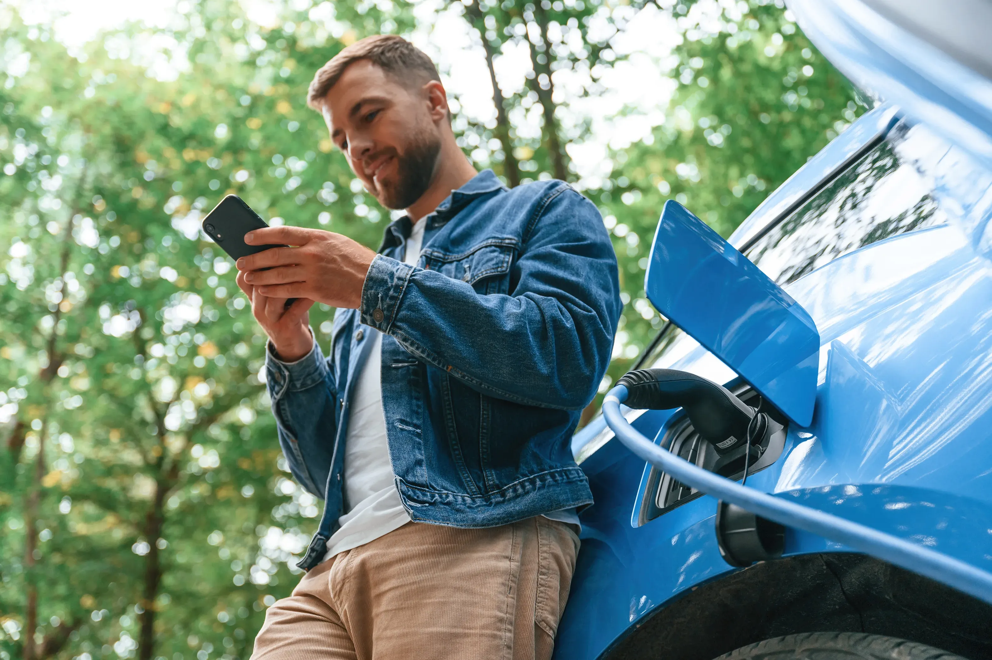 Uomo che tiene uno smartphone mentre ricarica un veicolo elettrico.