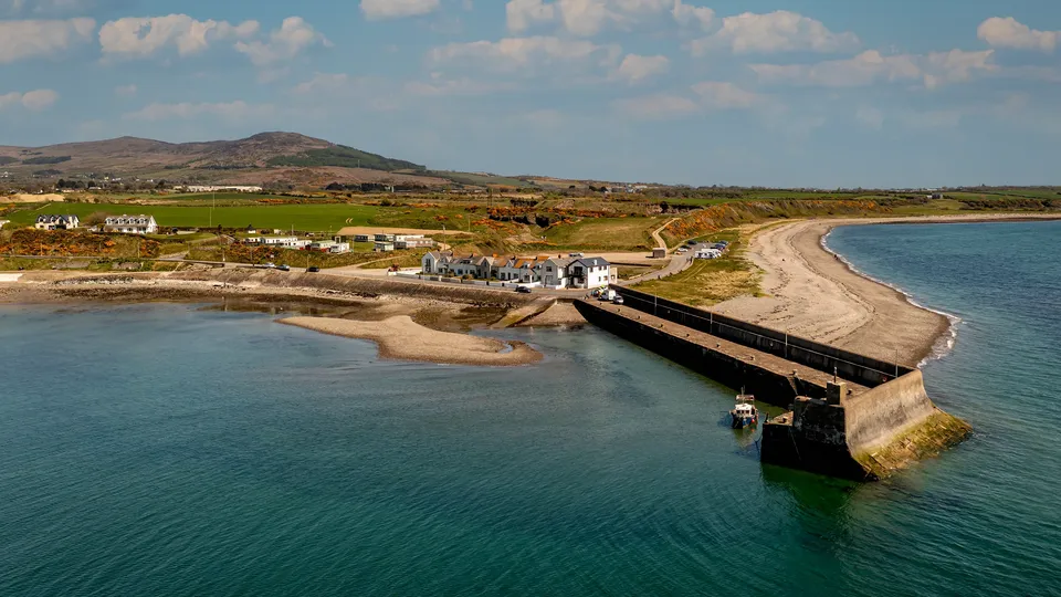 Aerial view of a coastal pier and sandy beach near Dundalk, with green fields and mountains in the background