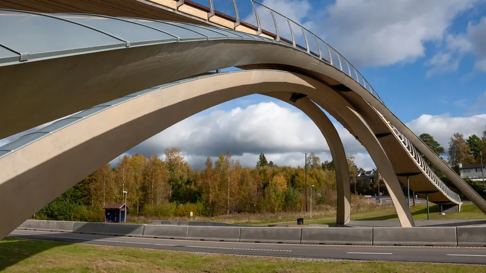 Buet fotgjengerbru med buede betongstøtter som spenner over en vei.