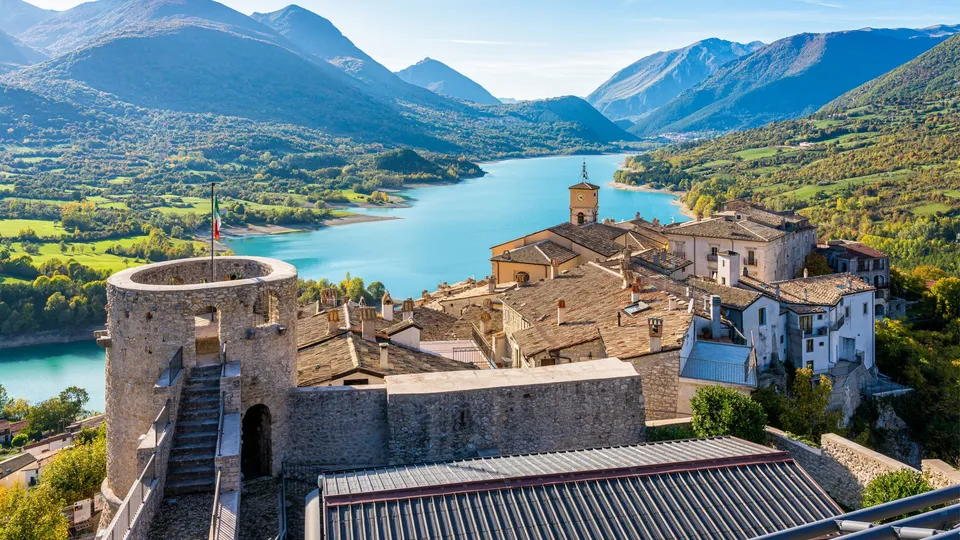 Fortezza medievale in pietra che domina un lago turchese circondato da montagne.
