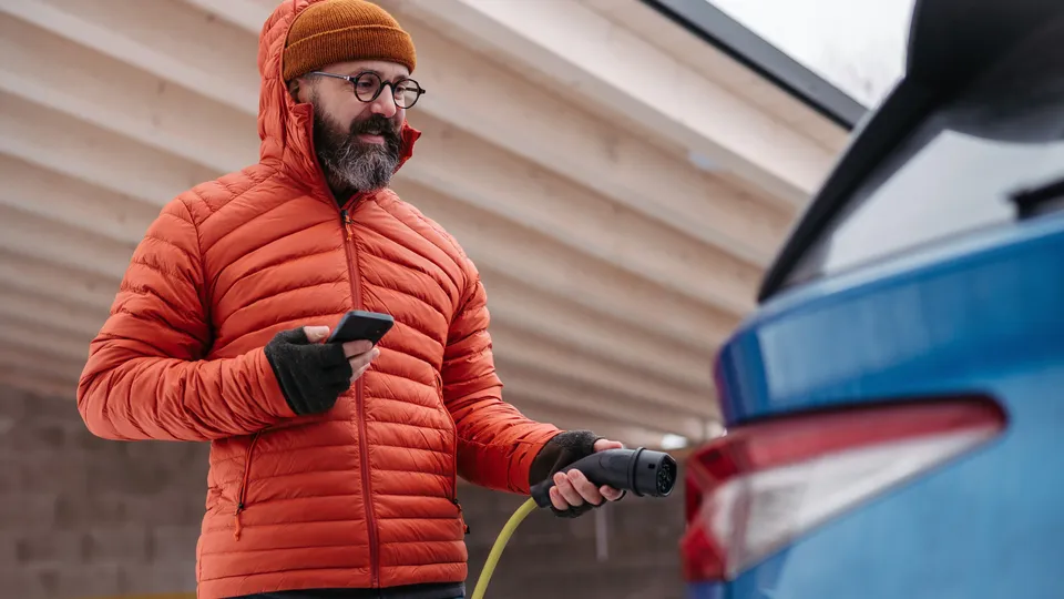 Mann som holder AC-lader ved siden av sin elbil