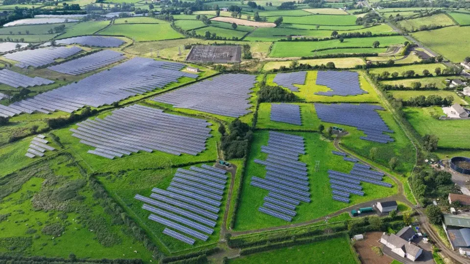 Aerial view of solar panel arrays across green farmland with hedgerows.