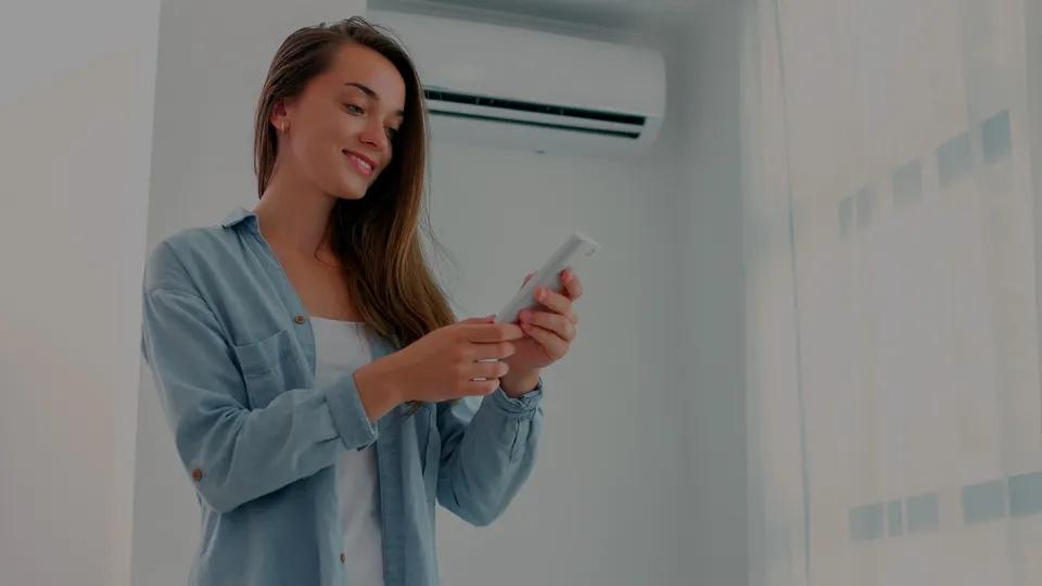 Mujer sosteniendo un control remoto mientras mira una unidad de aire acondicionado.