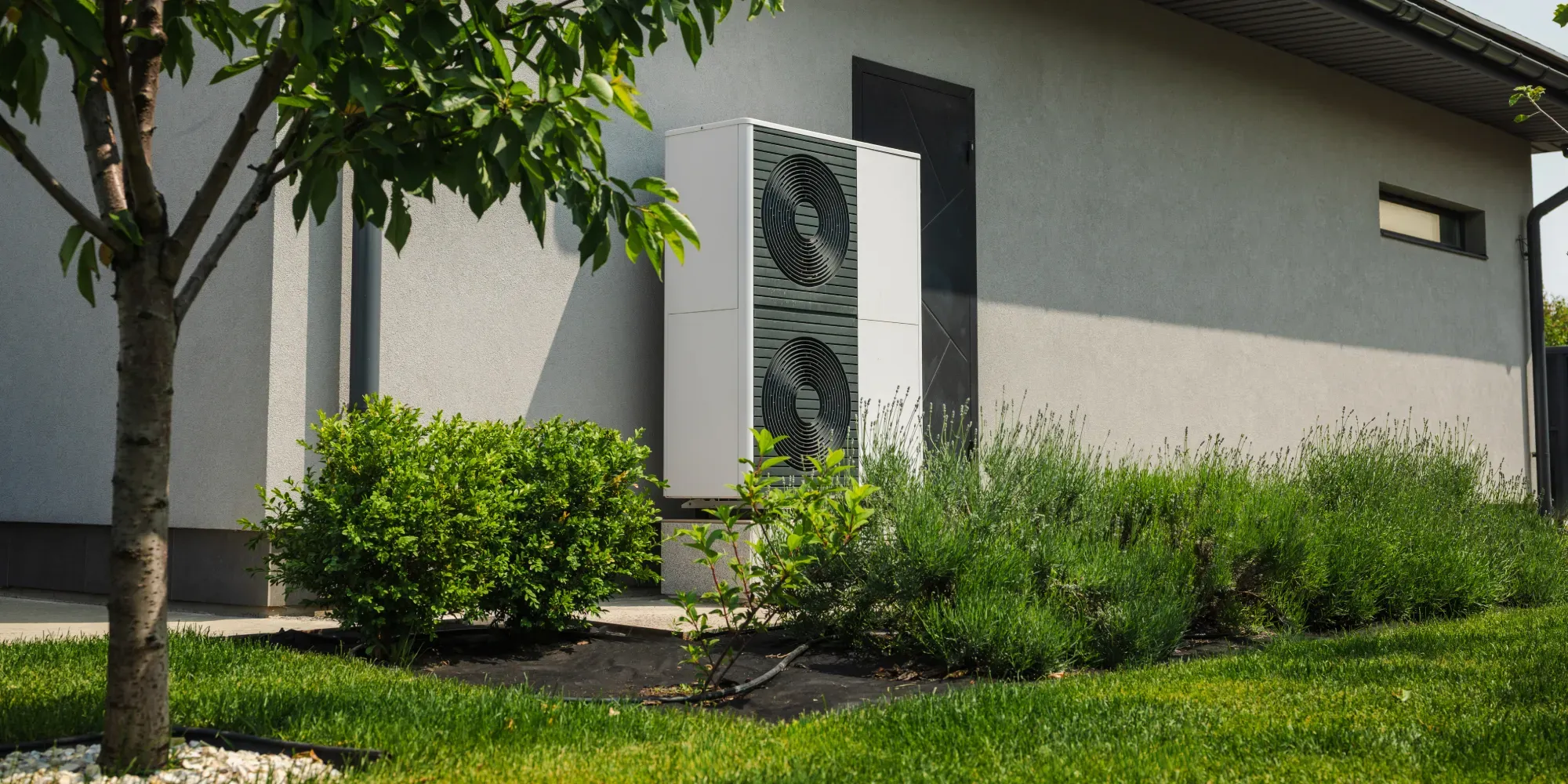Heat pump unit installed on modern house exterior with landscaping.
