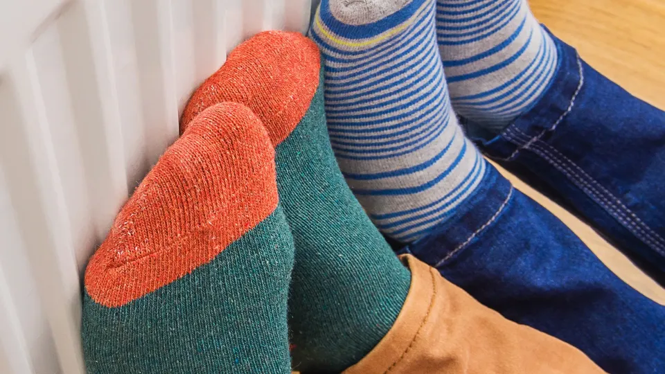 Due persone si scladano i piedi contro un termosifone indossando calze colorate.