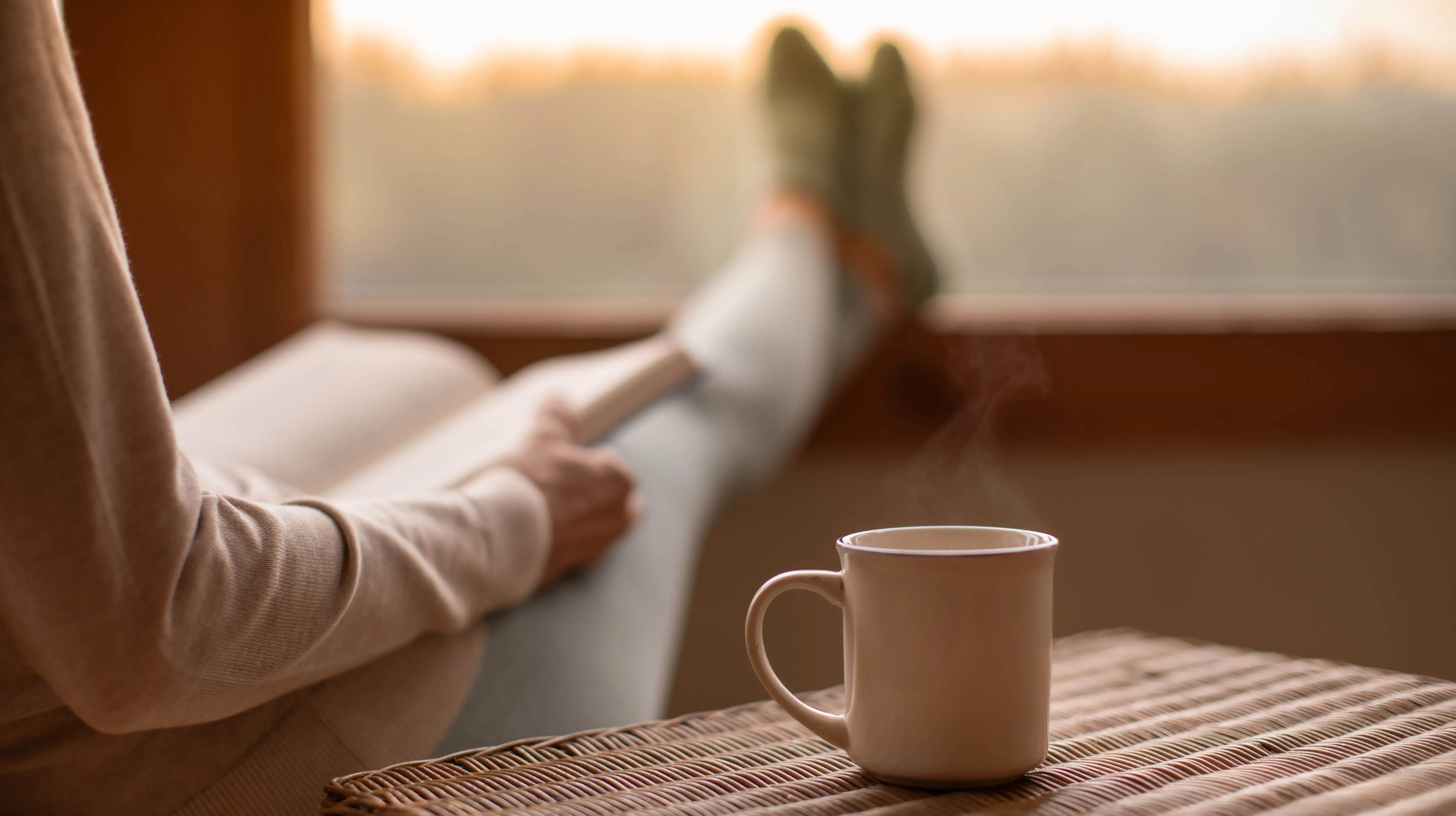 Person relaxing by window with coffee mug on table.
