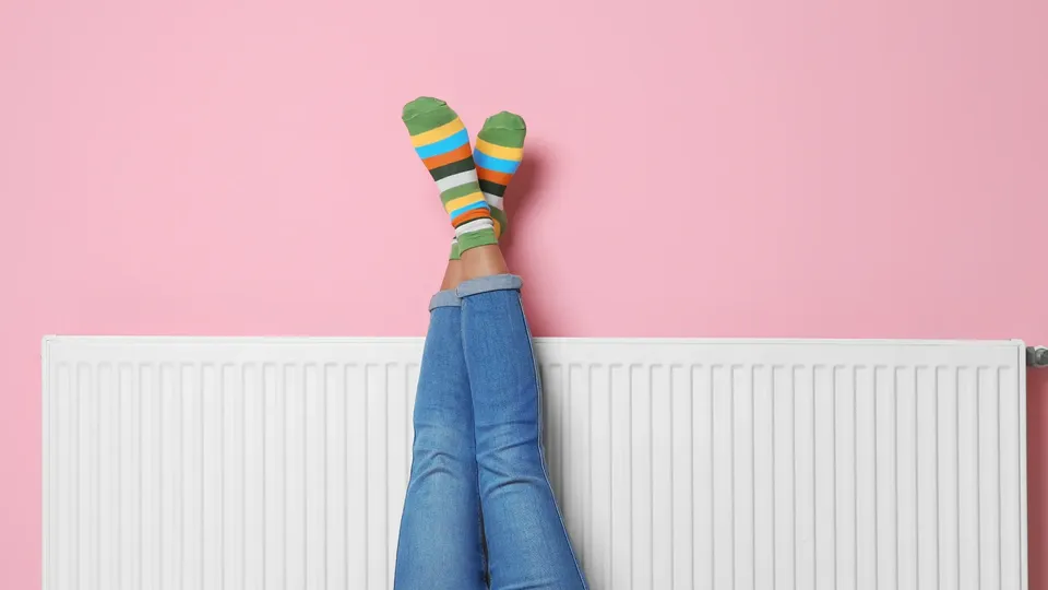 Persona con las piernas apoyadas contra el radiador, usando calcetines de rayas coloridas.