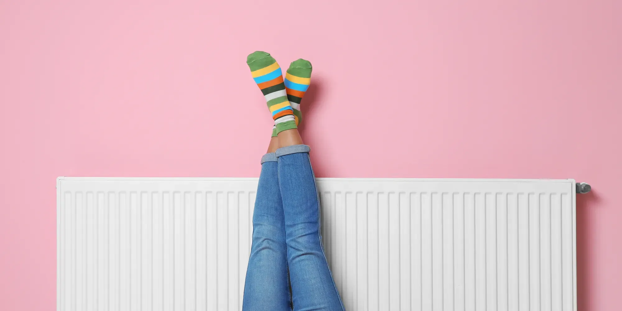 Persona con las piernas apoyadas contra el radiador, usando calcetines de rayas coloridas.