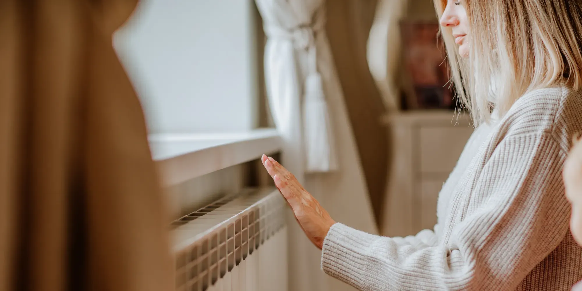 Woman adjusting a radiator valve on a wall-mounted heating unit.