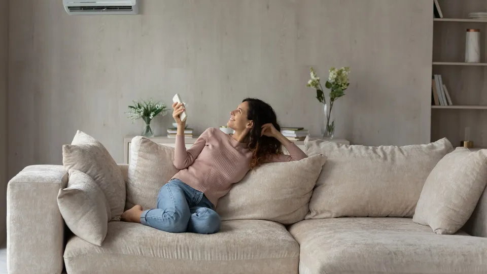 Kvinne på sofa holder fjernkontroll mot varmepumpe