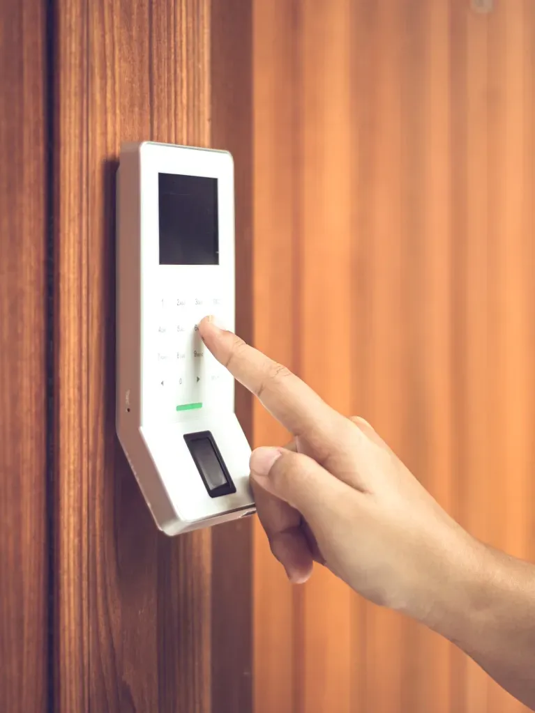 Person's finger pressing a white security keypad on wooden door.