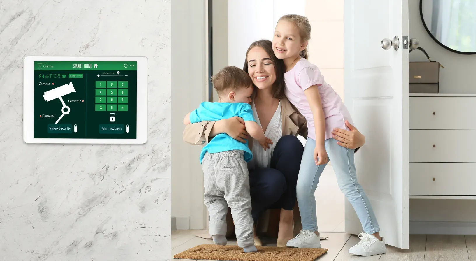 Woman with two children smiling next to smart home security control tablet on wall.