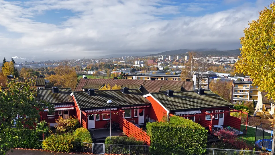 Eiendomsmegler Alna: Røde boligbygninger med byhorisont i bakgrunnen på høsten.