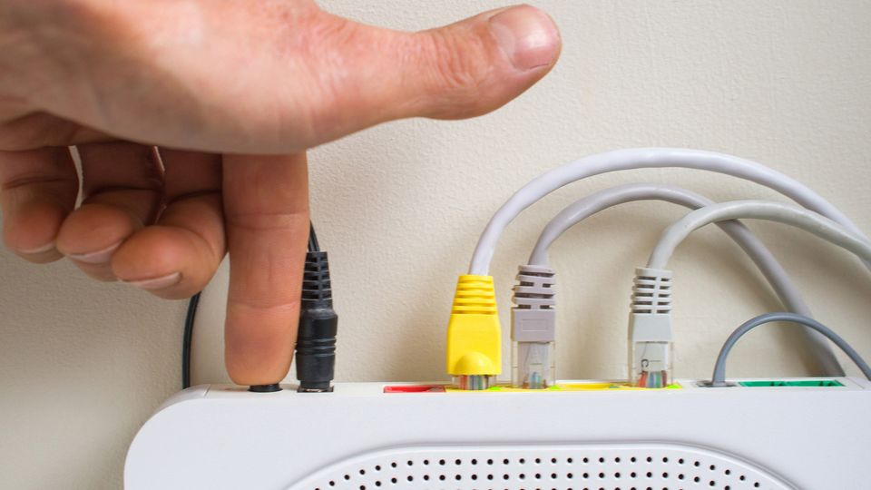 Nærbilde av oversiden av en en hånd som trykker inn reset-knappen på en router.