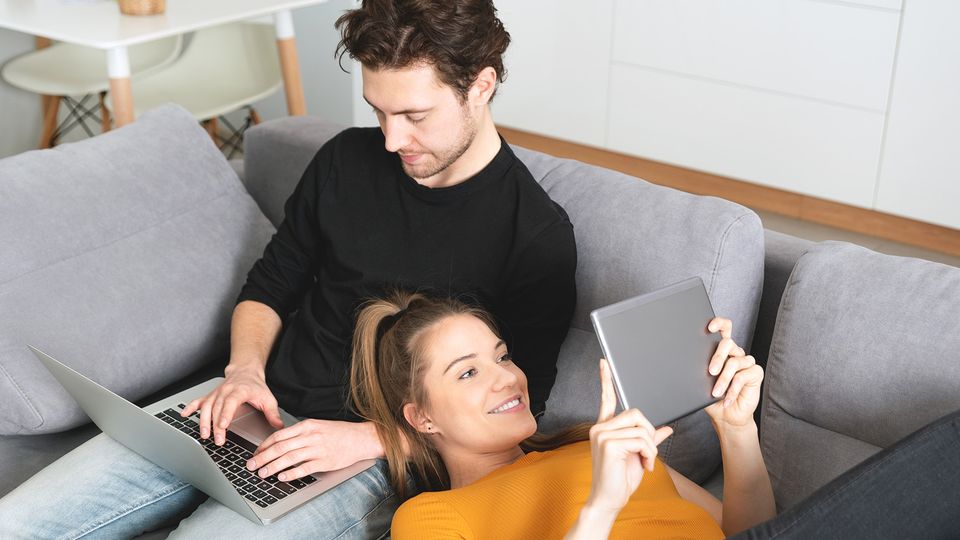 Bilde av et ungt par som sitter i en sofa på hver sin skjerm.