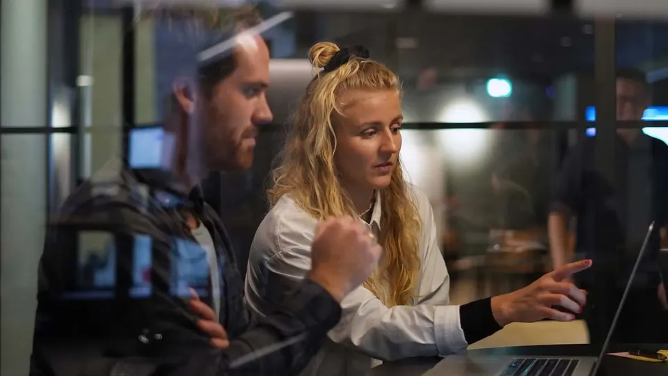 Kvinne gesturerer mot laptopskjermen mens mann ser på ved siden av henne.