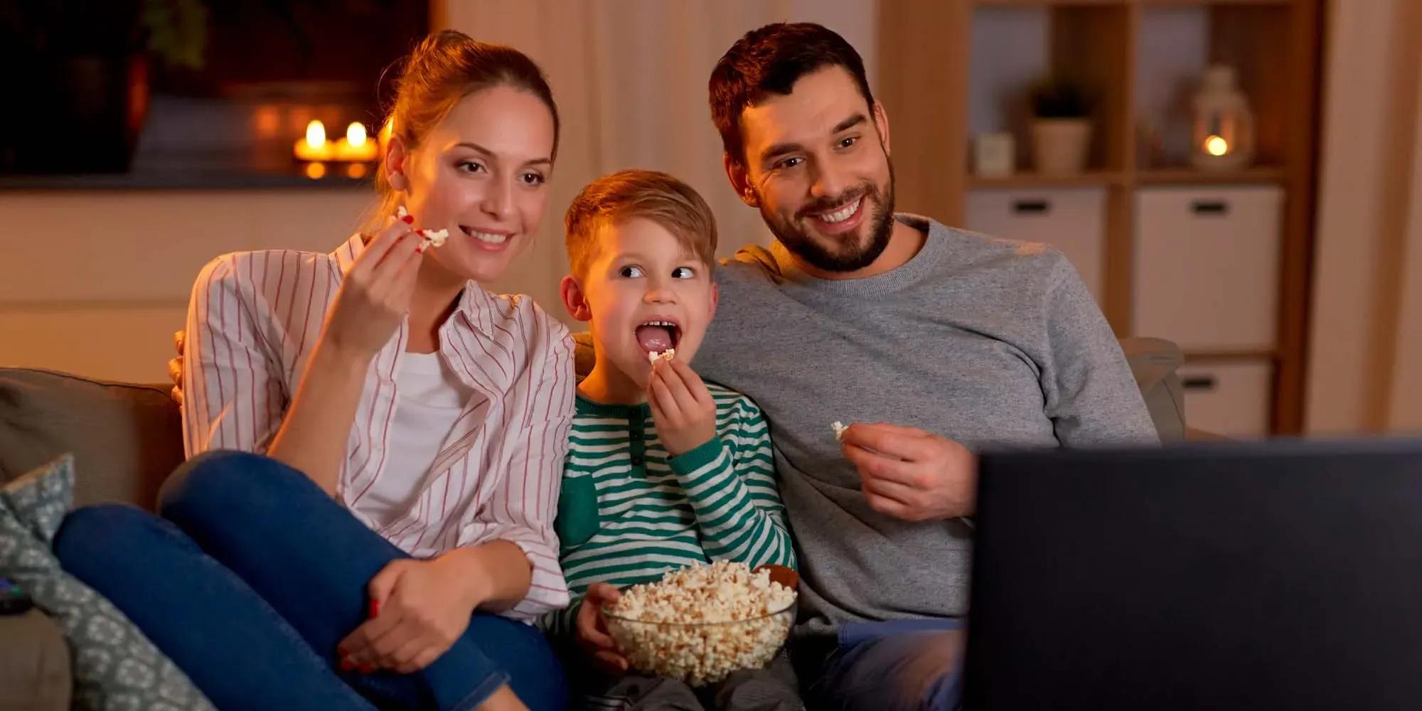 Familia comiendo palomitas mientras mira una laptop juntos.
