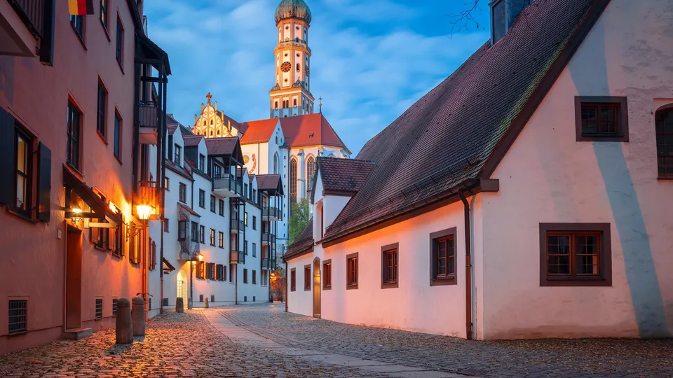 Altstadtgasse in Augsburg mit Kopfsteinpflaster und Kirchturm in der Abenddämmerung