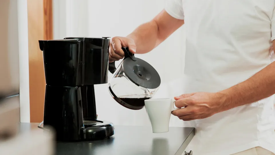 En man häller upp kaffe från en kaffebryggares kanna.