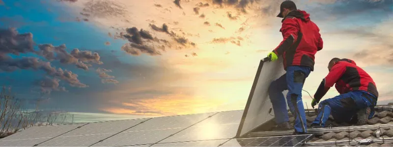 Trabalhadores instalando painéis solares num telhado ao pôr do sol.