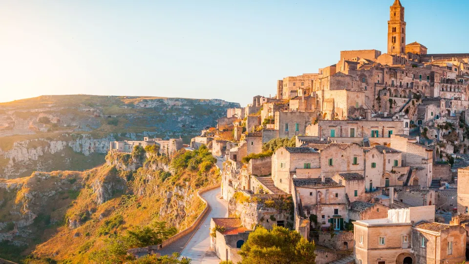 Antico borgo collinare con edifici in pietra e campanile che si affaccia su una valle fluviale sinuosa.