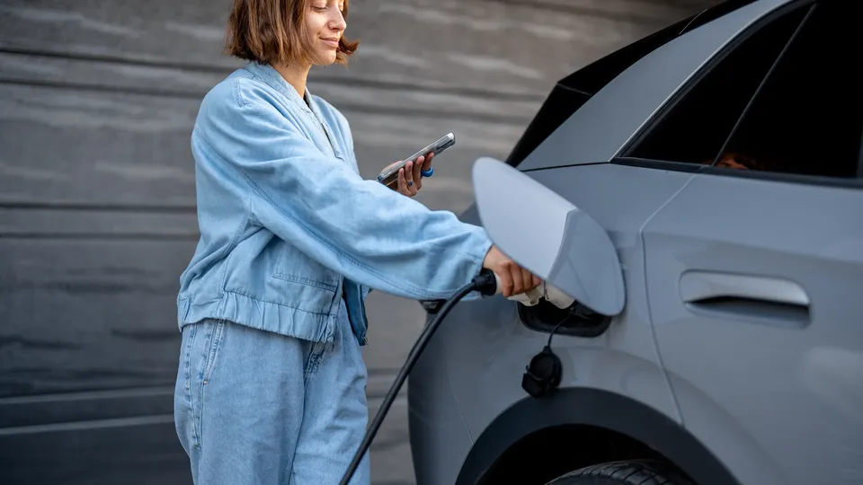 A woman checking her phone as she effortlessly chargers her grey EV.