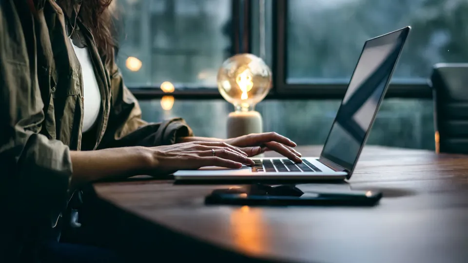 Person skriver på bærbar computer ved skrivebord med tændt pære.