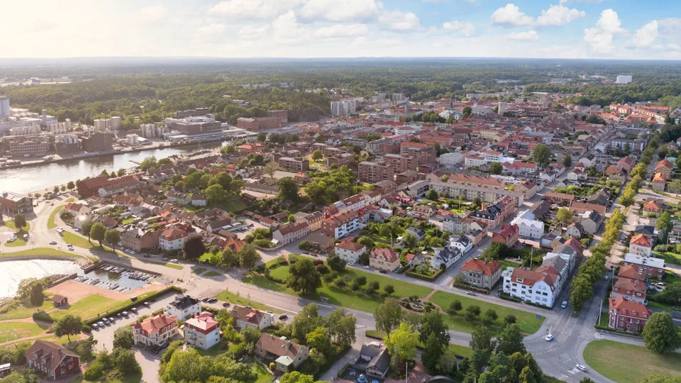 Flygfoto över Karlshamn med bostadshus, båthamn och skogslandskap.
