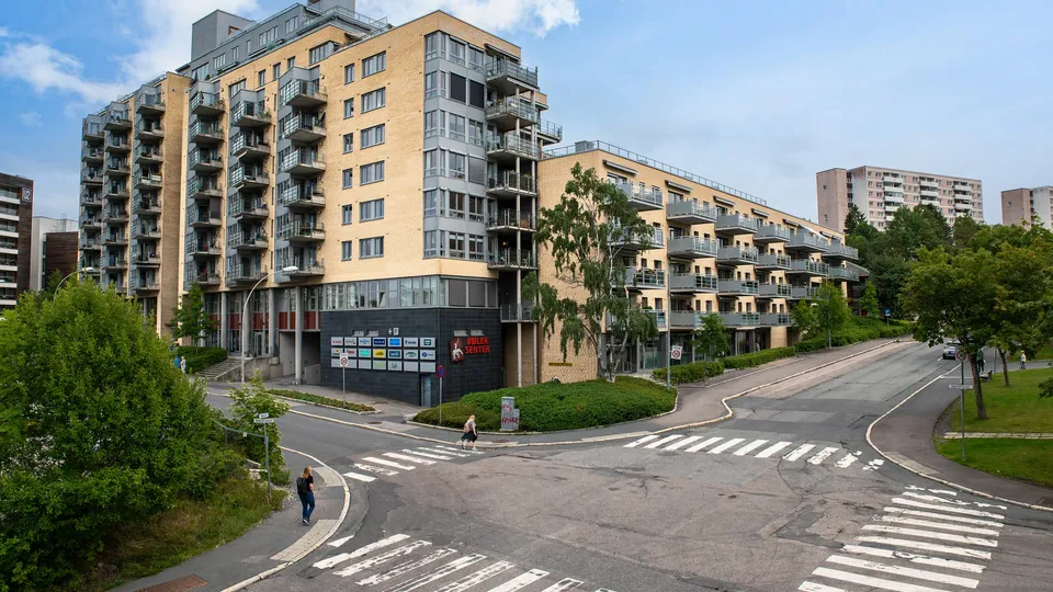 Moderne leilighetsblokker med balkonger ved et urbant kryss med fotgjengere som krysser.