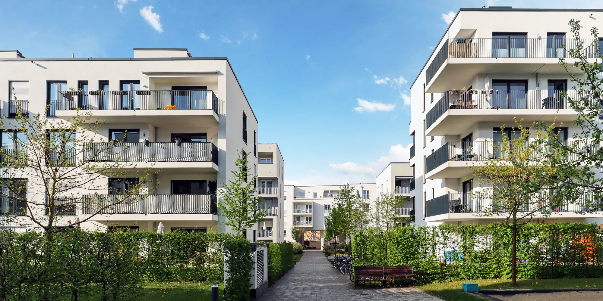 Moderne lejlighedsbygninger med altaner omkring en baggård.
