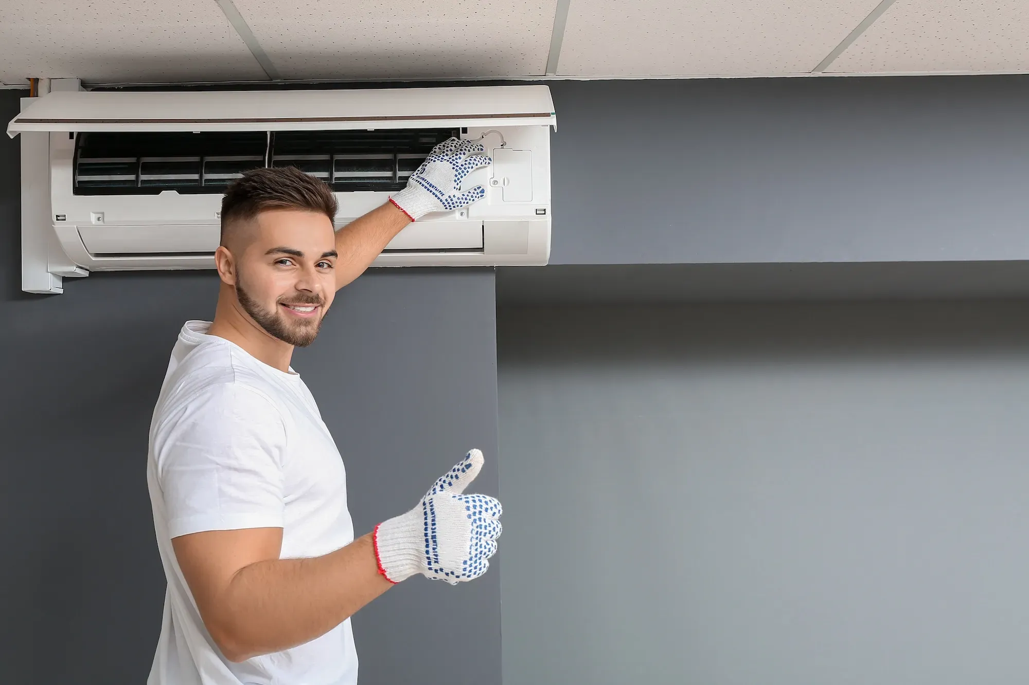 Tecnico con guanti da lavoro che effettua manutenzione su un'unità di condizionamento d'aria a parete.