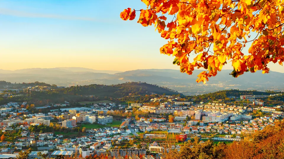 Folhagem de outono emoldura uma cidade em encosta com montanhas ao longe.