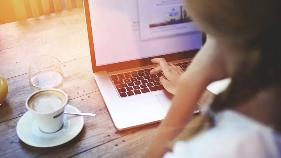 Person skriver på bærbar computer ved træbord med kaffe og juice.