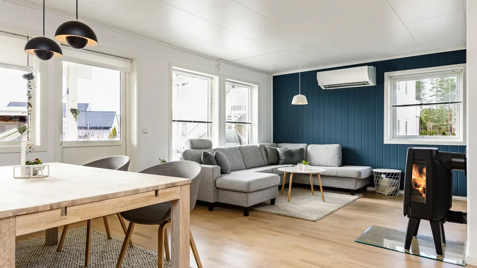Moderne stue med grå seksjonssofa og sort vedovn, og varmepumpe