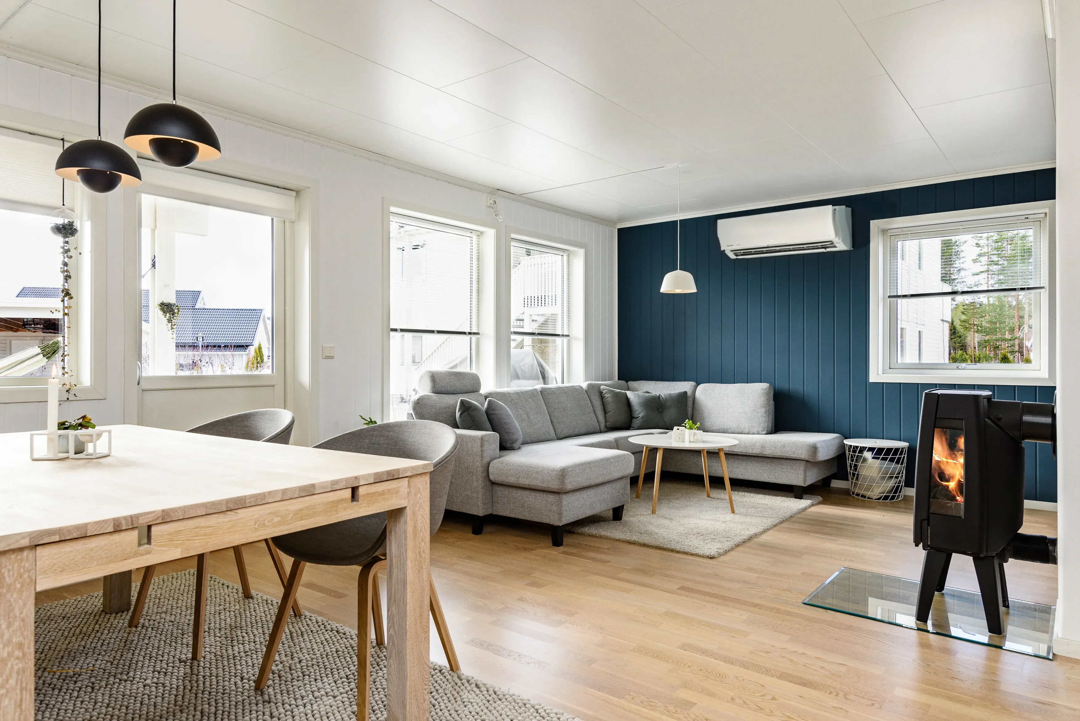 Moderne stue med grå seksjonssofa og sort vedovn, og varmepumpe