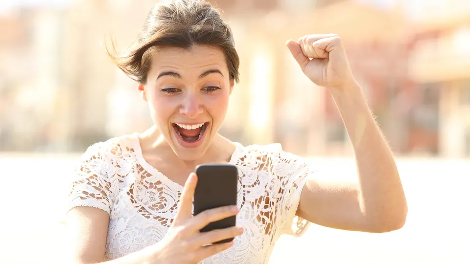 Woman looking at phone with fist raised in celebration.