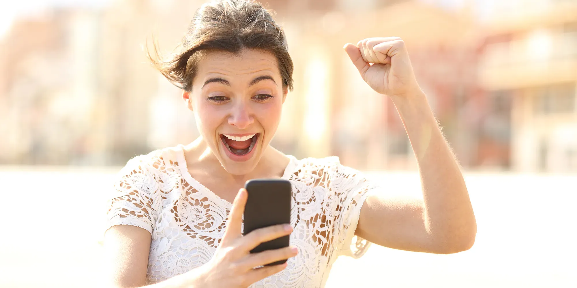 Woman looking at phone with fist raised in celebration.
