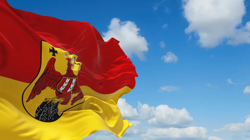 Rot-gelbe Flagge des Burgenlandes mit dem burgenländischen Wappen vor blauem Himmel mit Wolken.