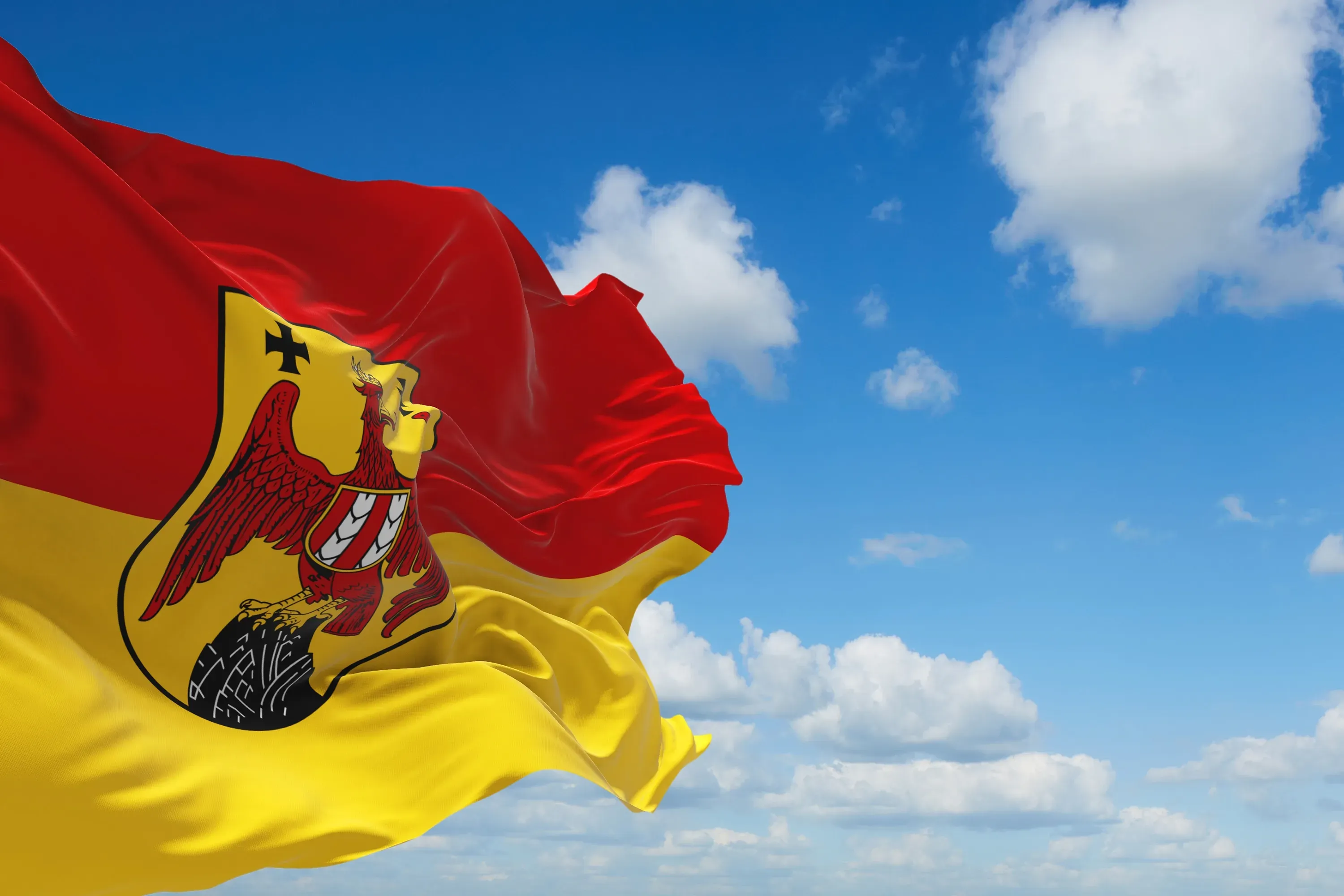 Rot-gelbe Flagge des Burgenlandes mit dem burgenländischen Wappen vor blauem Himmel mit Wolken.