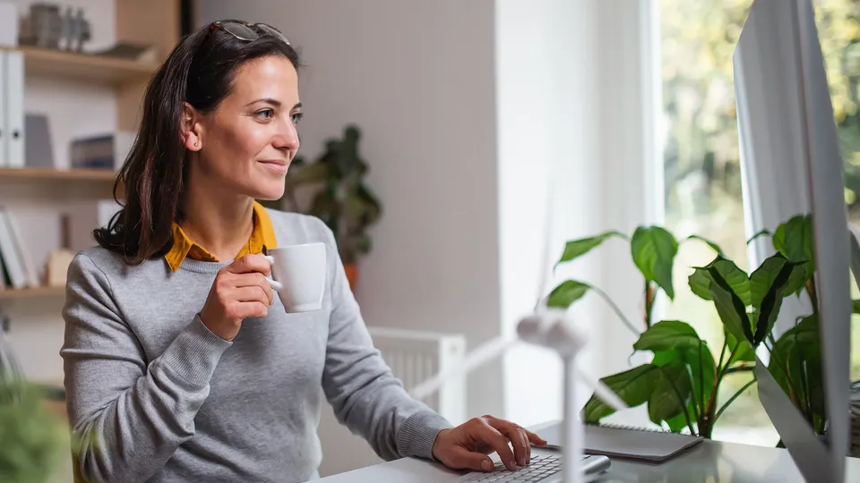 Kvinne ved skrivebord holder kaffekrus mens hun ser på dataskjerm