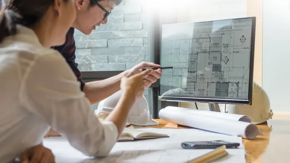 Kvinne peker på arkitekturtegning på skjerm mens hun gjennomgår byggeplaner.