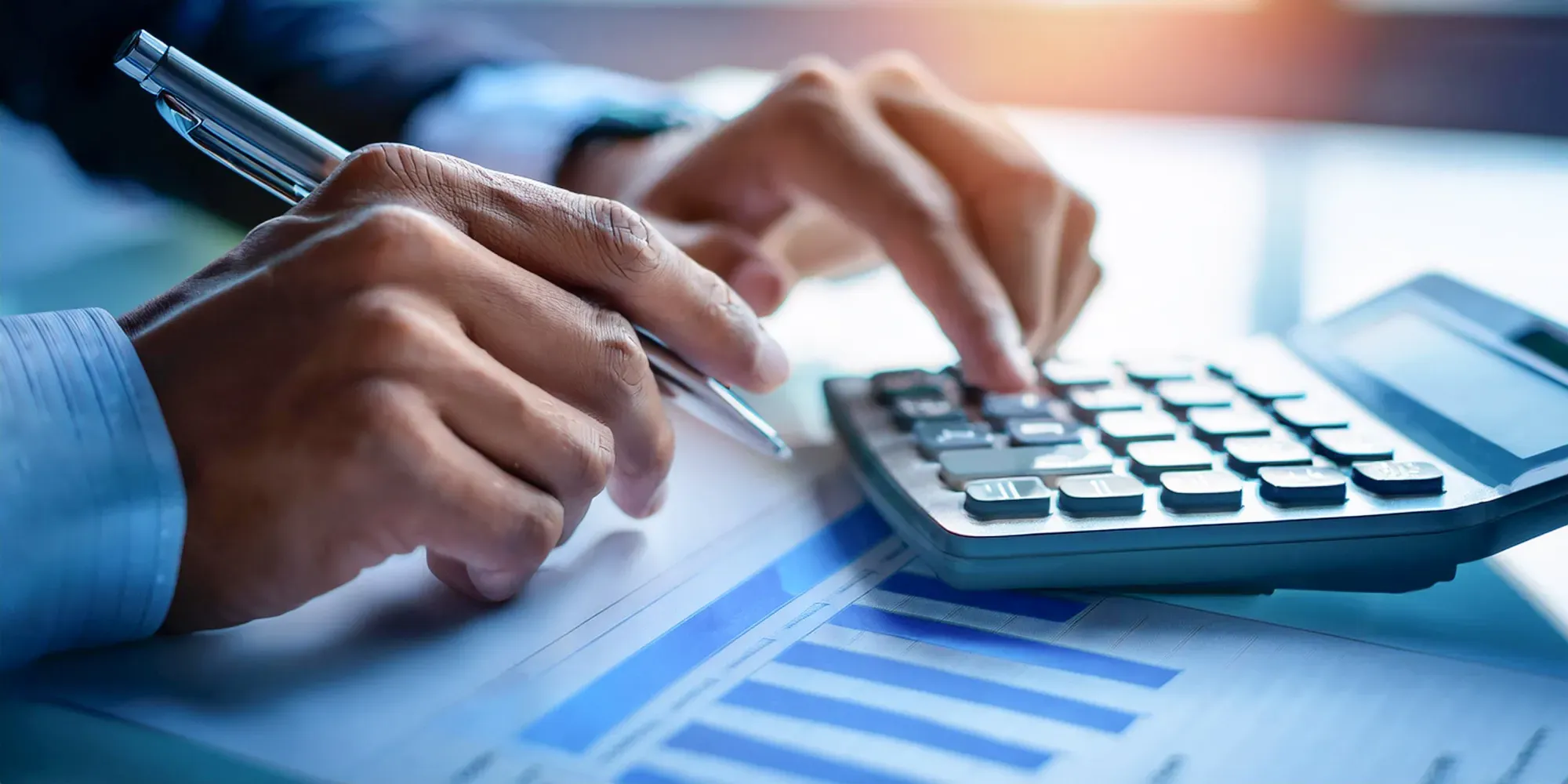 Persona sosteniendo un bolígrafo y usando una calculadora mientras revisa documentos financieros.