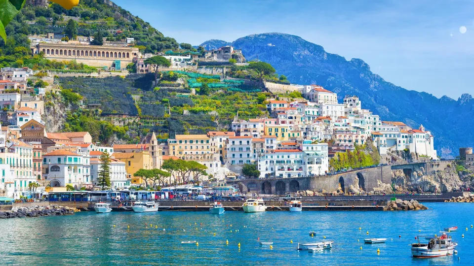 Villaggio costiero colorato arroccato su scogliere sopra acque turchesi del Mediterraneo con barche.