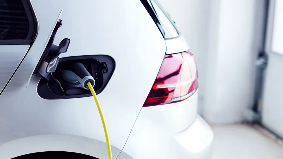 Close-up of a yellow charging cable plugged into a white electric vehicle in an indoor parking space