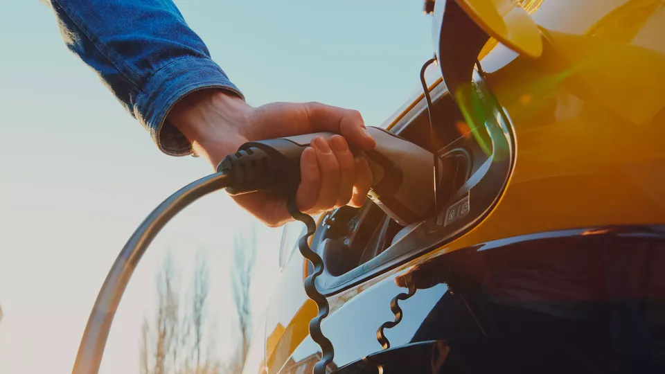 Hand holding electric vehicle charging cable connected to yellow charger.