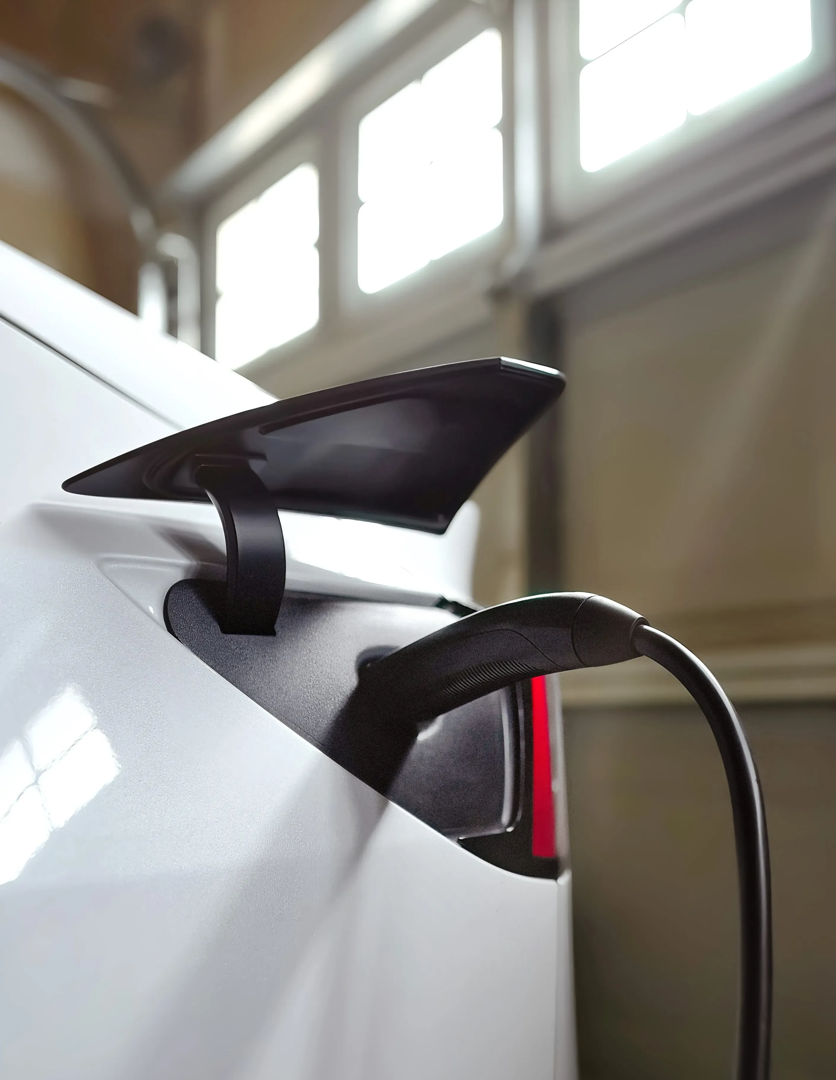 Electric vehicle charging cable plugged into white car with roof-mounted charger.