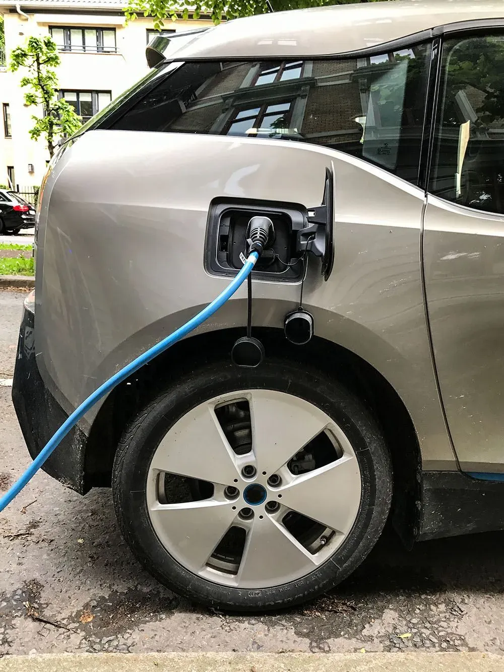 Veicolo elettrico grigio in ricarica con cavo blu collegato alla porta di ricarica.